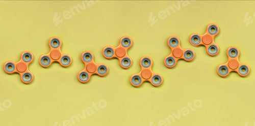 Preview: Many orange fidget spinners lies on texture background of fashion pastel orange color paper