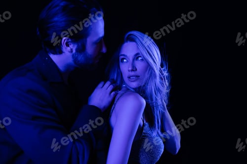 Preview: Young man touching seductive blonde girlfriend with blue lighting isolated on black