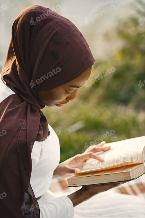 Preview: Portrait of a muslim woman sits on the plaid picnic blanket near the river