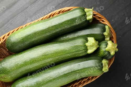 Preview: Fresh ripe zucchinis in wicker basket on black table, top view