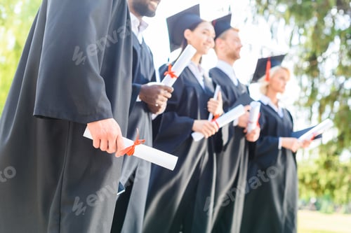 Preview: cropped shot of graduated students in capes and hats holding rolled diplomas