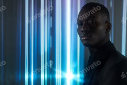 Preview: Young serious businessman in black formalwear standing against striped background