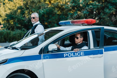 Preview: middle aged policemen in sunglasses walking out from car at urban street