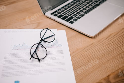 Preview: business documents, eyeglasses and laptop at wooden workplace