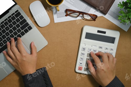 Preview: Overhead view of female accountant making calculations and using laptop at desk