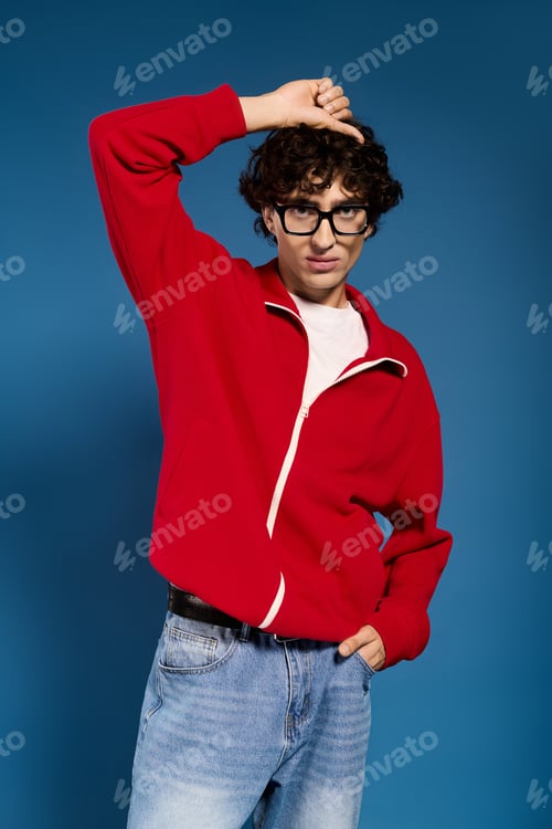 Preview: Young stylish man showcases modern fashion against a vibrant blue backdrop in a relaxed pose