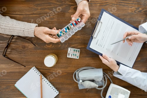 Preview: Overview of hands of sick senior man holding container with pills over table