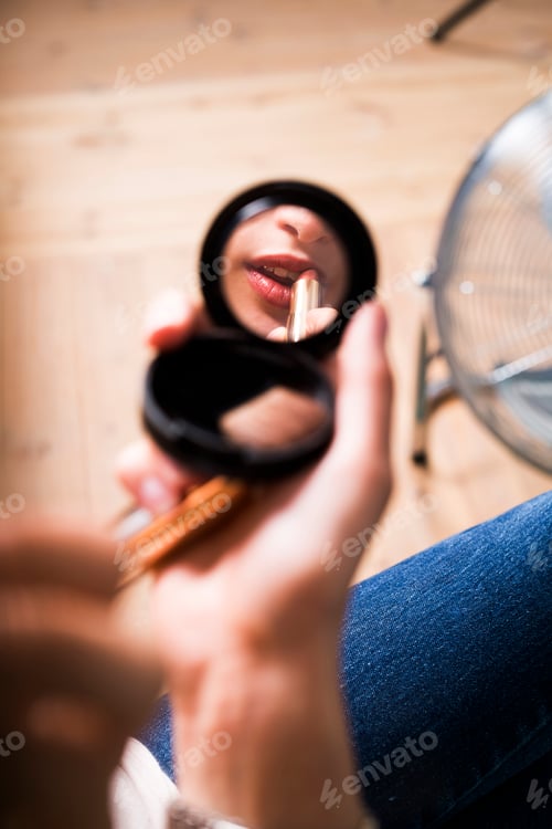 Preview: Reflection of fashion model applying lipstick in mirror at studio