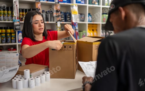 Preview: Young latin amercian woman working in retail, packaging a box for a client
