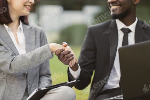Preview: Handsome African businessman and caucasian businesswoman in gray suit shaking hands together