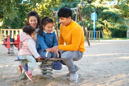 Preview: Hispanic family with two children playing together in a playground.