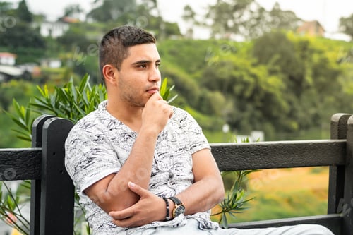 Preview: young Latino man, thinking and looking for new ideas, sitting on a chair in an outdoor park.