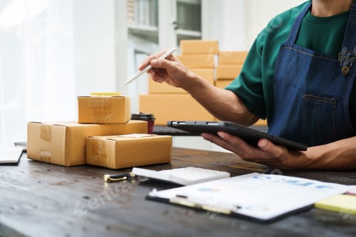 Preview: A man is working at his desk, preparing parcel boxes for shipment. He checks packs items carefully
