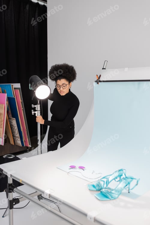 Preview: african american content producer in eyeglasses near spotlight and stylish sunglasses with sandals