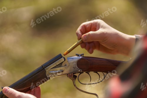 Preview: Close-up of hunter man charges the cartridge on rifle gun in forest.