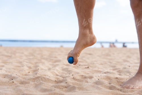 Preview: Man doing foot massage with small ball on beach sand