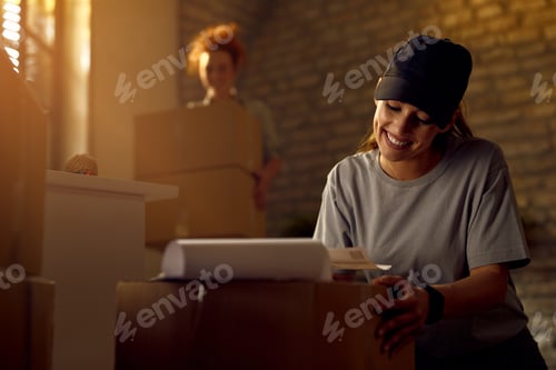 Preview: Happy female courier preparing package for delivery while working in the office.