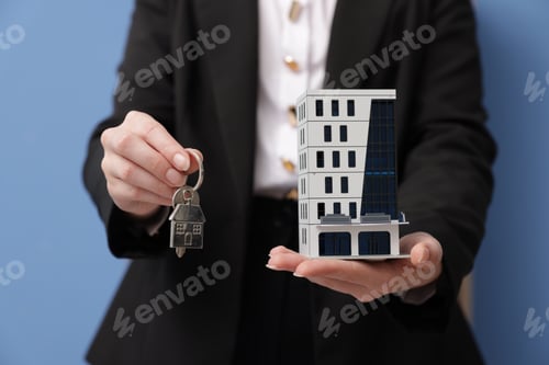 Preview: Real estate agent holding house model and key in office, closeup