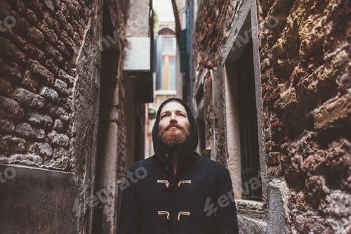 Preview: Mid adult man in hooded duffle coat staring from alley, Venice, Italy