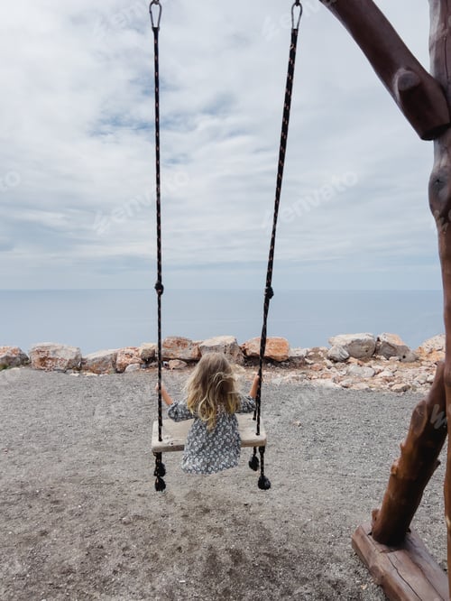 Preview: Little girl swings on a rope swing on a mountain above the sea