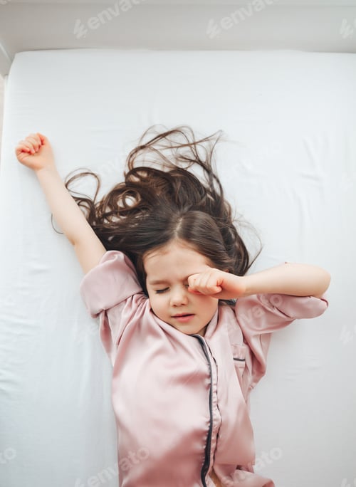 Preview: Top view of a cute little girl stretching in a white bed, waking up in the morning.