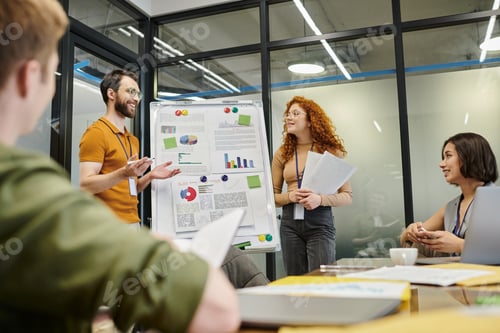Preview: smiling bearded businessman talking near graphs on flip chart near creative team in meeting room
