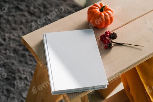 Preview: High angle view of white hard cover book on wooden decorative ladder with a pumpkin and red berries