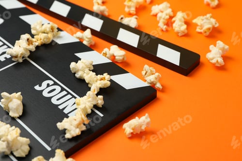 Preview: Clapperboard and popcorn on orange background. Food for watching cinema
