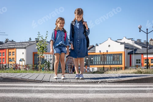 Preview: Two little girls with backpacks on the background of the school.