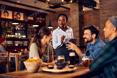 Preview: Happy African American waitress taking order from group of guests in a pub.