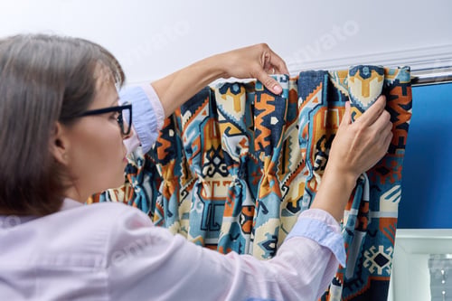 Preview: Woman hanging velvet curtains on metal hooks on cornice pipe