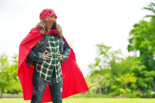 Preview: Happy girl are playing superhero. Kid run across green field in red cloak