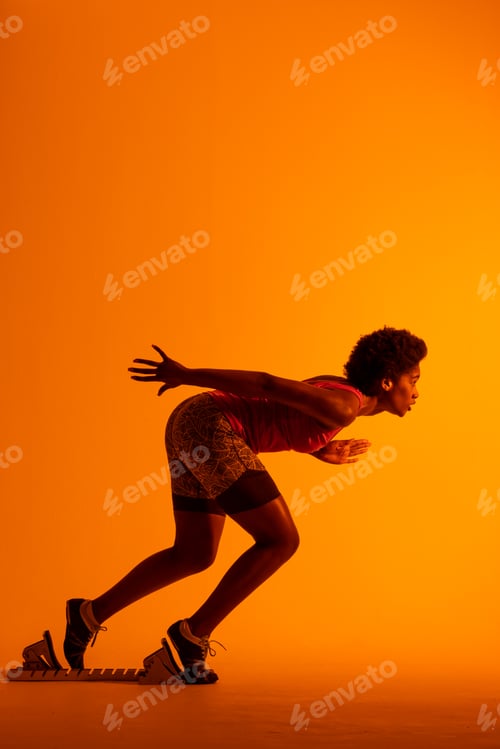 Preview: Vertical image of african american female athlete preparing for run in neon orange lighting