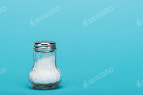 Preview: glass salt shaker full of salt on blue background with copy space