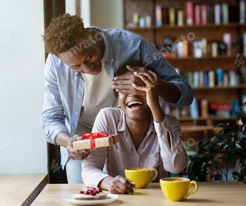 Preview: Affectionate black man surprising his beloved woman with Valentine's Day gift at coffee shop