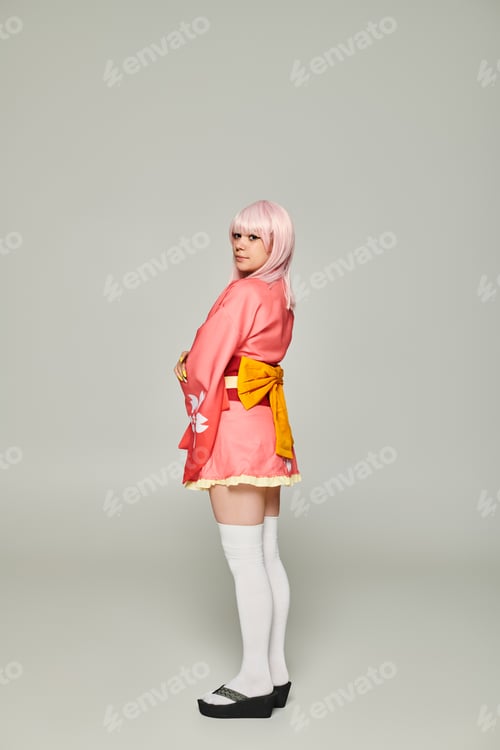 Preview: young anime style woman in blonde wig and pink kimono with yellow bow on grey, cosplay concept