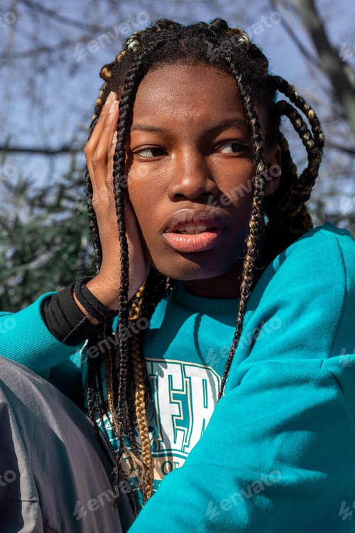 Preview: Young woman with dreadlocks styled in an intricate pattern sitting on a concrete ledge