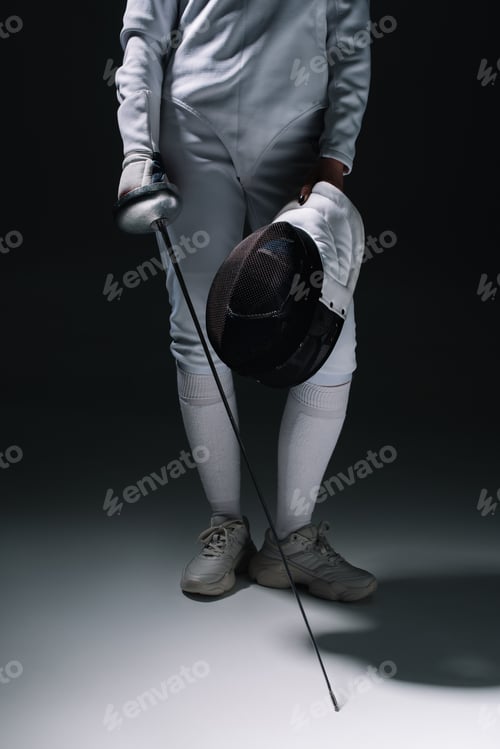 Preview: Cropped view of fencer holding rapier and fencing mask on white surface on black background