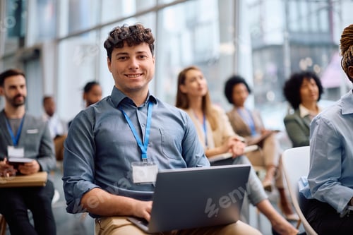 Preview: Happy businessman using laptop during a seminar in board room and looking at camera.