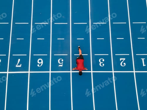 Preview: Aerial Drone View of Runner Crouched at Start Line on Blue Athletic Track