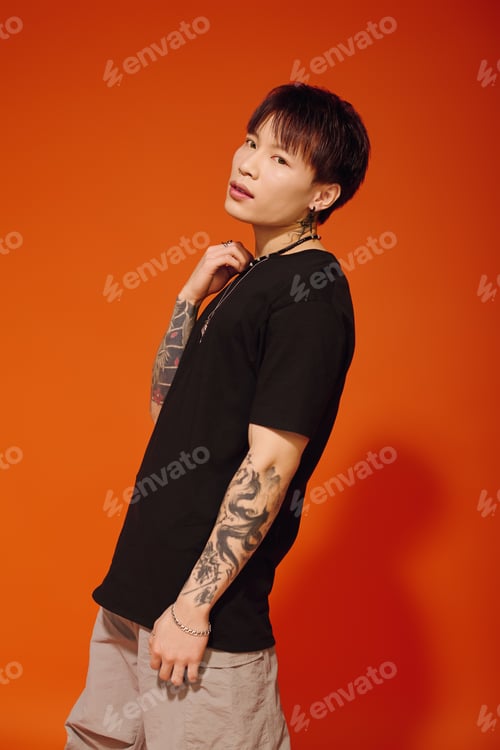 Preview: Stylish young asian man poses confidently against a vibrant orange backdrop