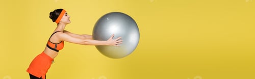 Preview: side view of sportive woman exercising with fitness ball isolated on yellow, banner
