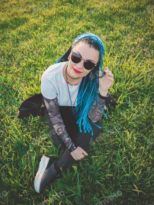 Preview: Stylish young beautiful woman with blue box african braids sitting on green grass in park
