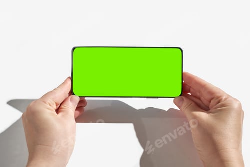 Preview: Female hands holding smartphone with green screen display on white background