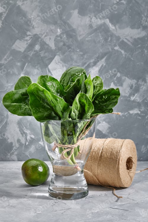 Preview: Bunch of fresh spinach leaves in a vase with water, gray background. Green leaves rich in trace