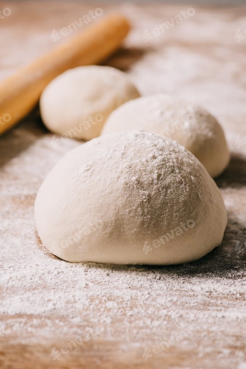 Preview: selective focus of raw dough for pizza and rolling pin on tabletop