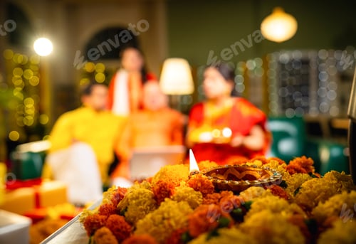 Preview: Closeup of glowing Diwali diya with blurred Indian family celebrating in festive home background