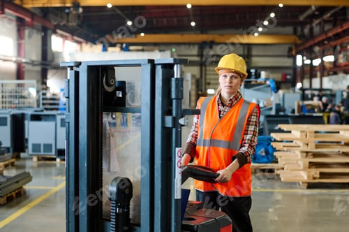 Preview: Young confident engineer in workwear standing in front of forklift in factory