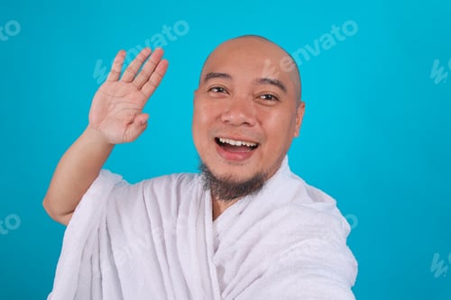 Preview: Cheerful Muslim Pilgrim in White Ihram Waving Hand for Selfie