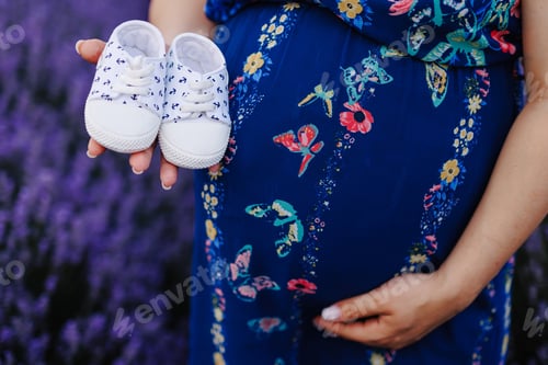 Preview: Close up of pregnant woman holding a pair of baby shoes